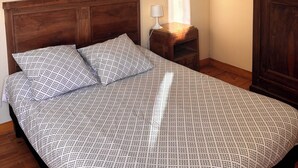 Een slaapkamer met een houten hoofdbord, een bed met beddengoed met een patroon, een nachtkastje met een lamp en een deur.