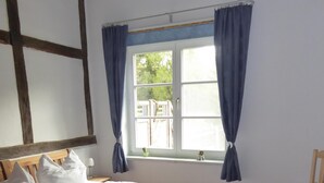 Una habitación con dos camas de madera, una ventana con cortinas, una silla y una lámpara en el techo.