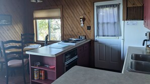 Una cocina compacta con paredes de madera, una ventana con persianas, un lavabo y electrodomésticos básicos.