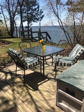 A deck with a round table and striped chairs, overlooking a lake.