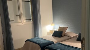 Ein Schlafzimmer mit zwei Betten, einem Nachttisch, einer Lampe und einem Fenster mit Vorhängen.