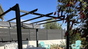 Ein Patio mit Pergola, weißen Plastikstühlen und einem Tisch.