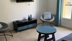 Ein modernes Wohnzimmer mit flachbildfernseher an der Wand, einem Sofa, einem runden Couchtisch und einem Beistelltisch mit dekorativen Vasen.
