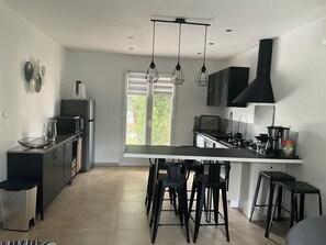 Een moderne keuken met een centraal eiland, barkrukken en een zwarte afzuigkap.