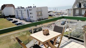 Een balkon met een tafel en stoelen, uitkijkend op een parkeerplaats en gebouwen.