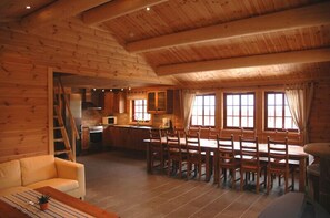 Interior de una cabaña de madera con comedor, cocina y sofá.