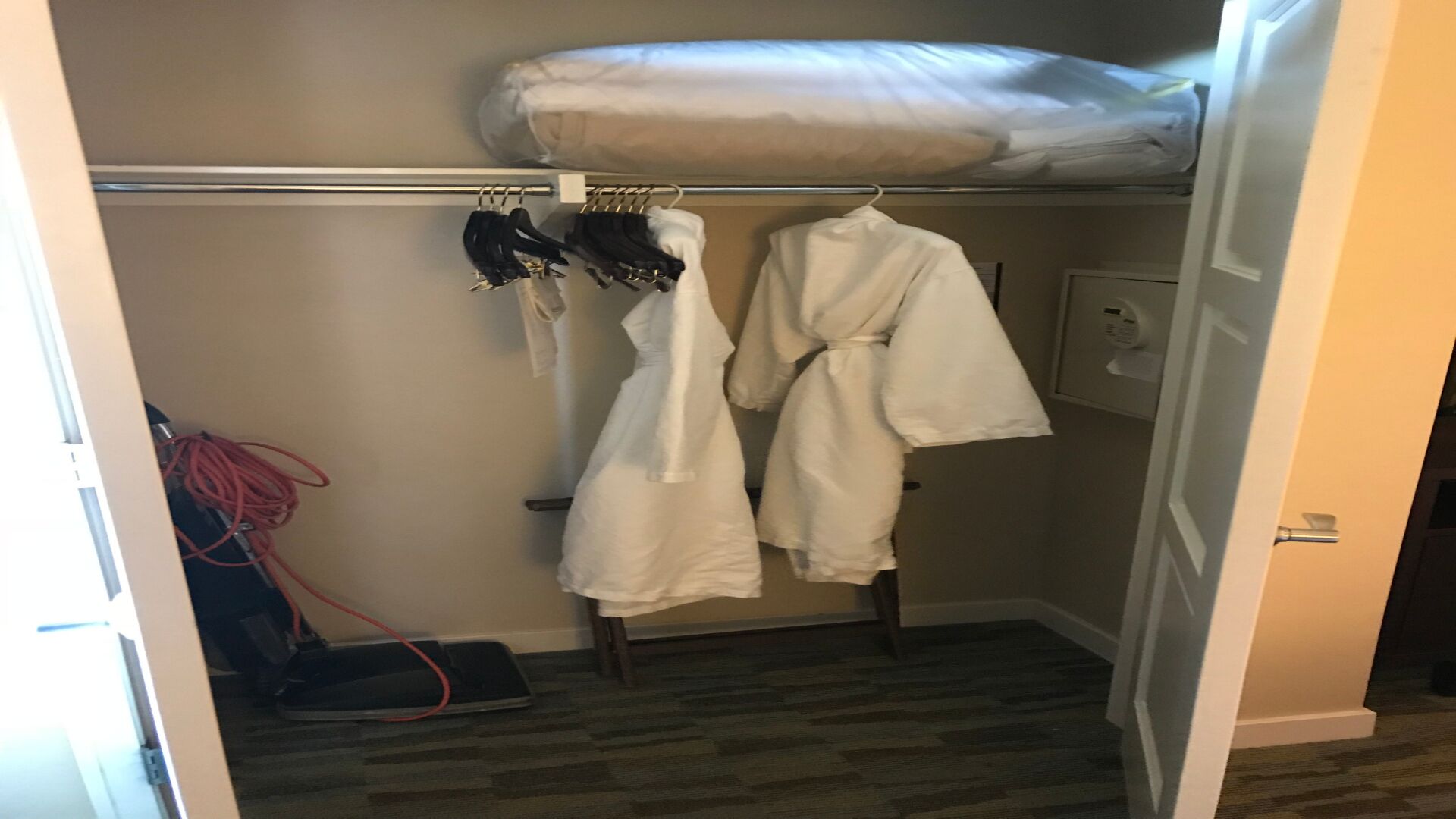 Une petite pièce avec un lit superposé, un porte-manteau avec deux peignoirs et un aspirateur.