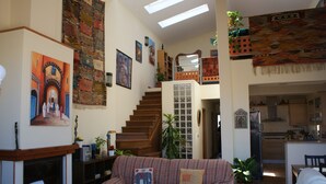 A cozy living room with a fireplace, a staircase, and a kitchen in the background.