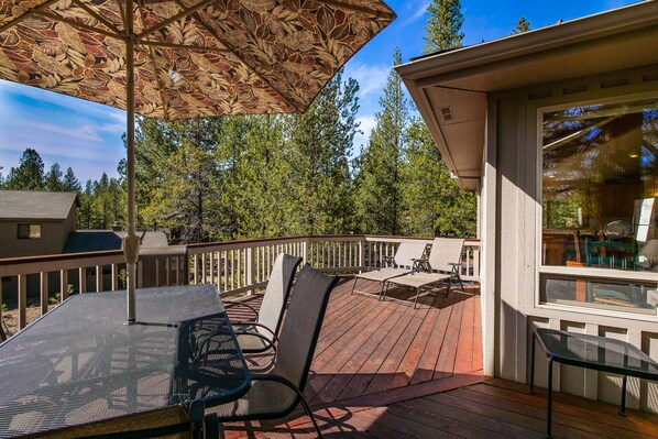 Une terrasse avec une table et des chaises, un parasol et une vue sur les arbres.