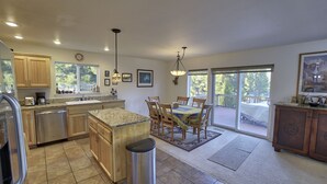 A spacious kitchen with granite countertops, wooden cabinets, and a large island. There is a dining area with a table and chairs, and a view of a deck through large sliding glass doors.