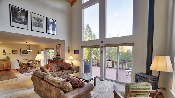 A spacious living room with a large sofa, a coffee table, and a fireplace. There are large windows and a balcony visible.