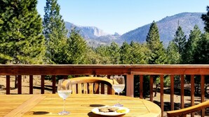 A wooden deck with a table set for two, overlooking a mountainous landscape.