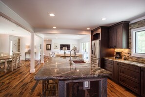 Kitchen features a central island with a granite countertop and stainless steel sink, complemented by dark cabinets and a stone backsplash.