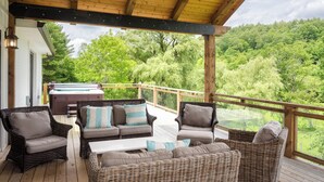 A covered deck with wicker furniture, a hot tub, and a view of a forested area. - 36 Private Acres on the New River (Boone)