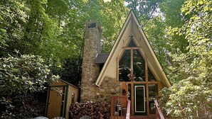 Una cabaña acogedora con chimenea de piedra, terraza de madera y sillones Adirondack.