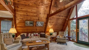 A cozy log cabin interior with a wooden ceiling, a sofa set, a coffee table, and a large window offering a view of the outdoors. - 2 Miles to National Park or Downtown Gatlinburg! Less than1/2 mile to Ober! (Gatlinburg)