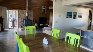 A spacious living room with a wooden floor, a dining table with green chairs, a fireplace, and a television.