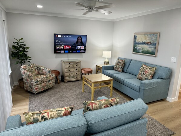 A living room with a blue sofa, floral armchair, and a television displaying Hulu content.