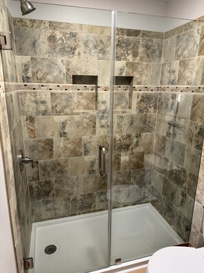 Un box de ducha con puerta de vidrio, paredes de azulejos y ducha.