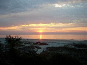 A sunset over a beach with a boardwalk and dunes.