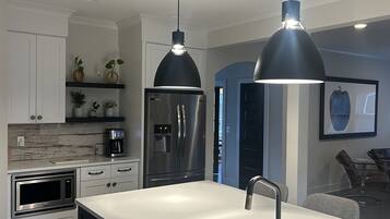 A modern kitchen with stainless steel appliances, white cabinetry, and pendant lighting.