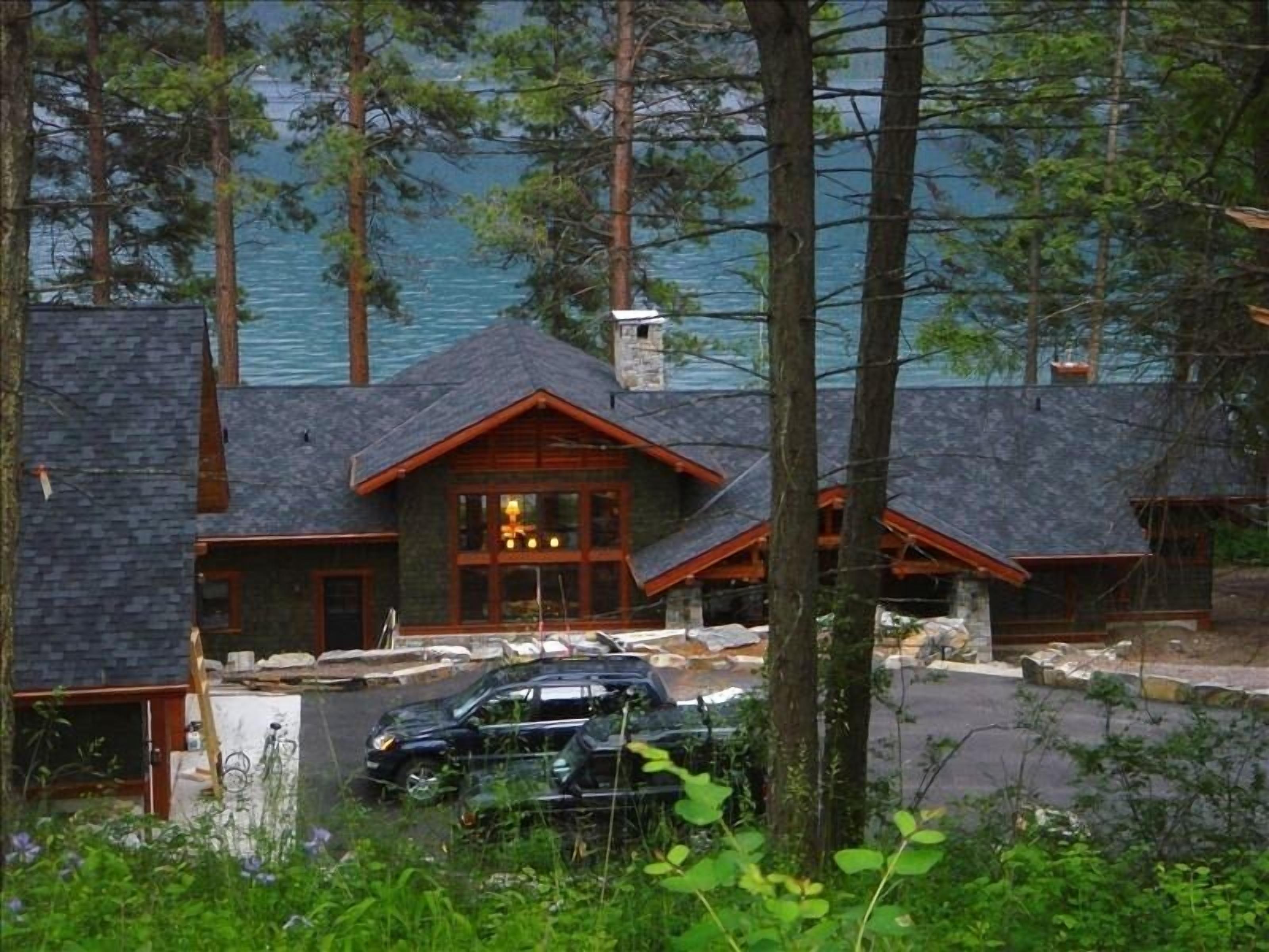 A lodge with a stone chimney, wooden exterior, and a view of a lake.