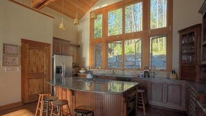 A spacious kitchen with a large island, wooden cabinets, and a stone countertop. - The Most Beautiful House on Flathead Lake - NW Travel Magazine 'Best Waterfront' (Polson)
