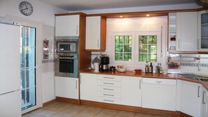 Cucina con pensili bianchi, forno integrato, macchina da caffè e finestra vista verde.