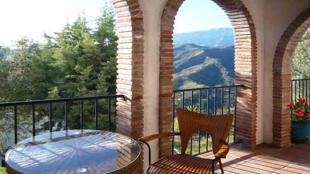 Un balcone con un tavolo in vetro e sedie in vimini, affacciato su un paesaggio montuoso.