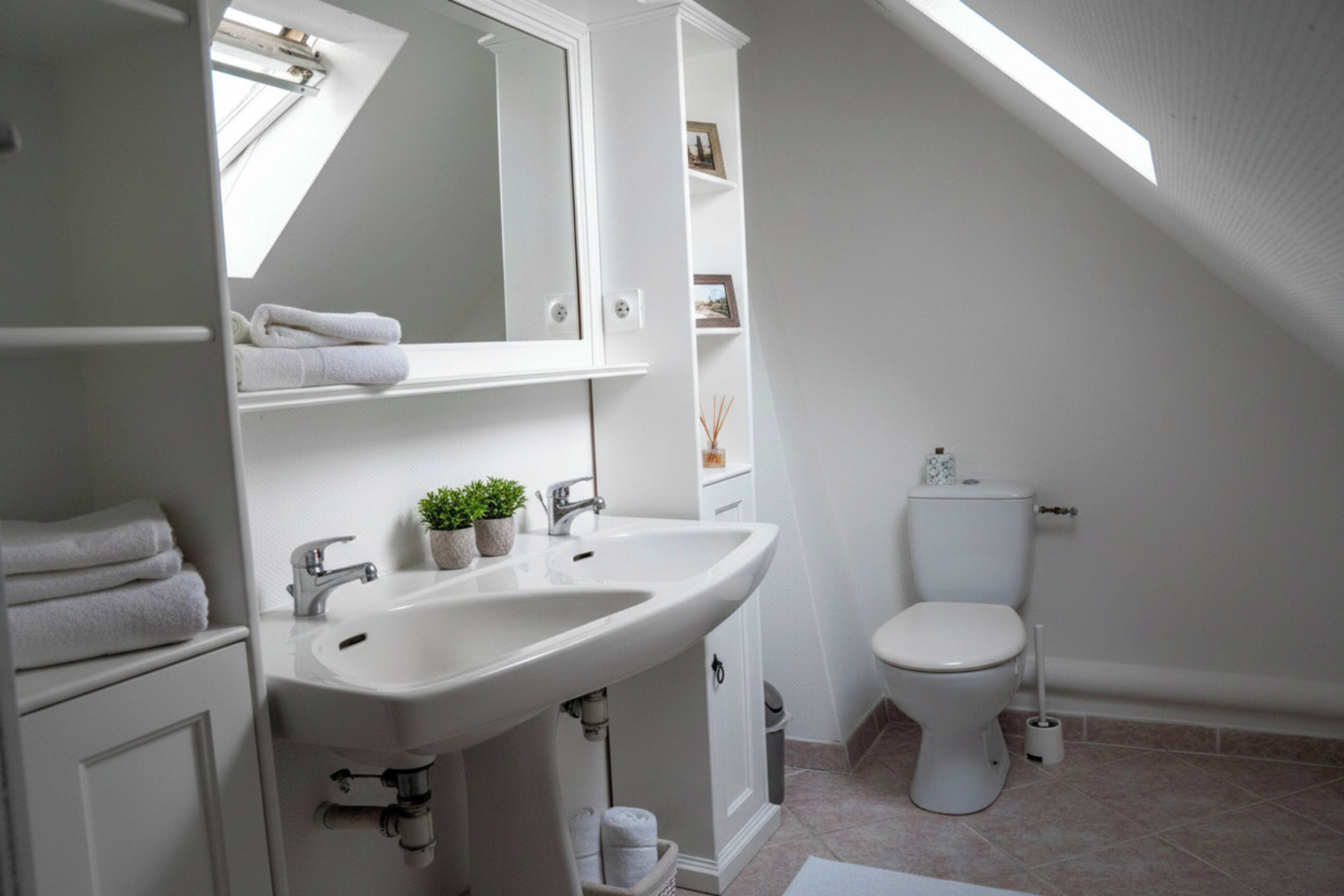 A modern bathroom with a white sink, mirror, and toilet, under a sloped ceiling.