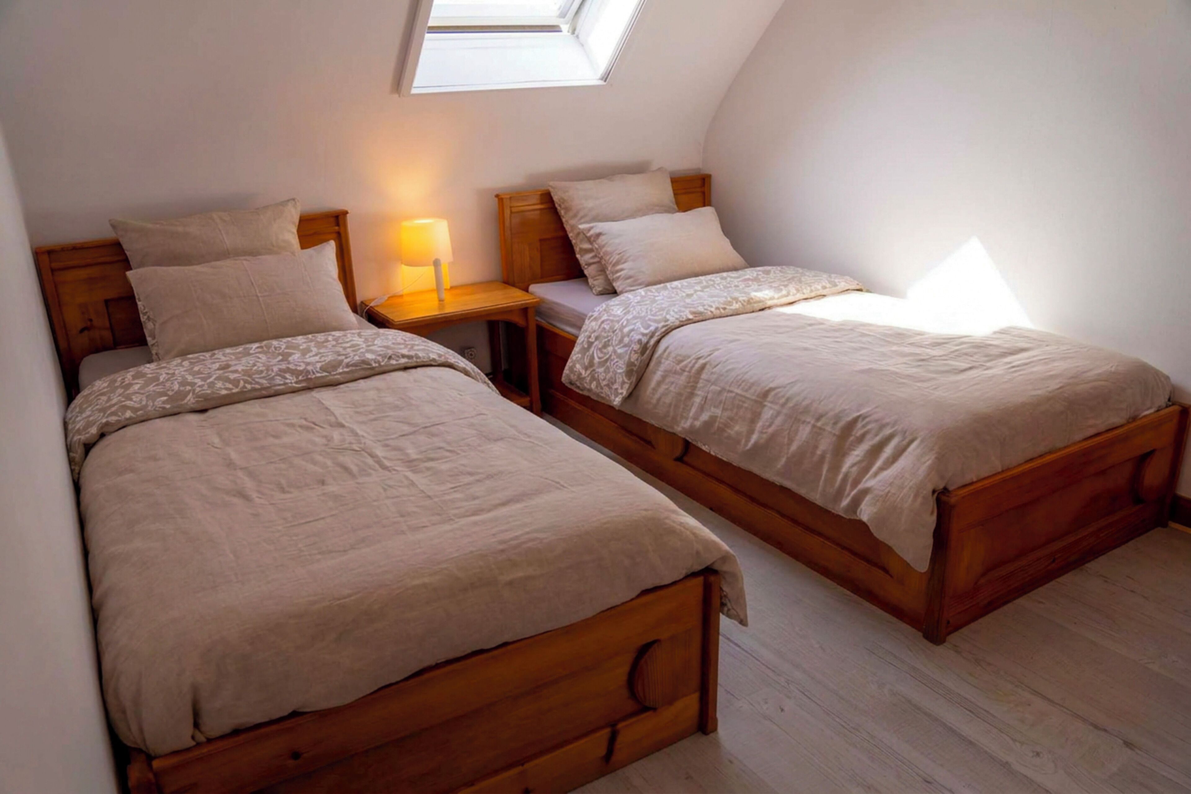 Une chambre avec deux lits en bois, une table de chevet avec une lampe et une lucarne.