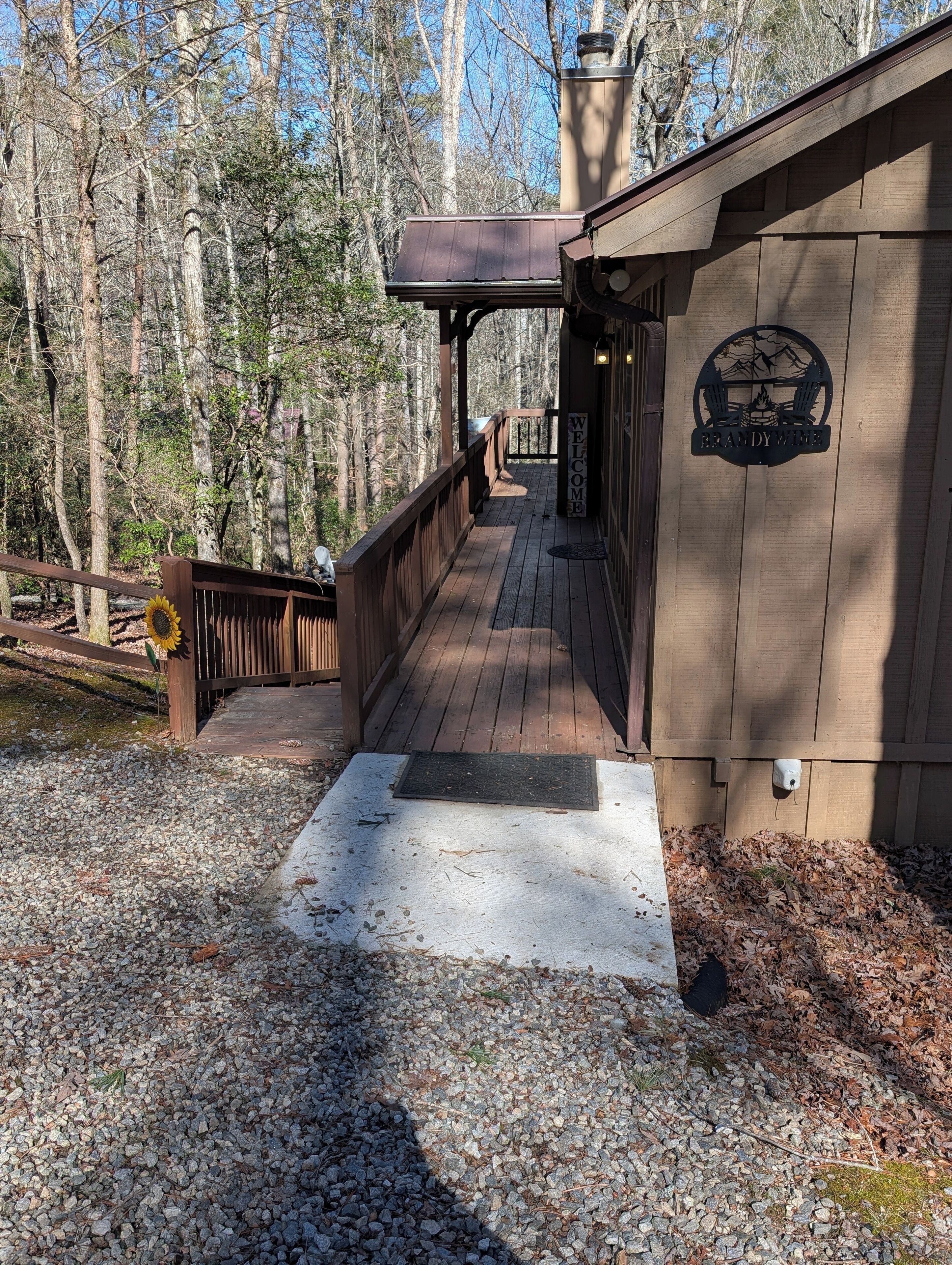 A wooden deck leading to a cabin with a 'Welcome' sign, surrounded by trees.