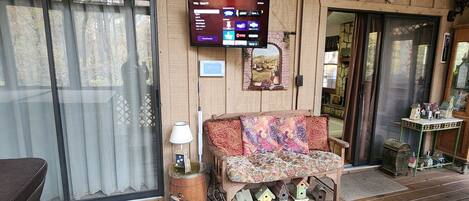A cozy room with a wooden interior, a sofa with patterned cushions, a television mounted on the wall, and a small table with decorative items.