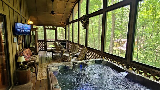 Eine Holzterrasse mit Whirlpool, Sitzbereich und Fernseher an der Wand.