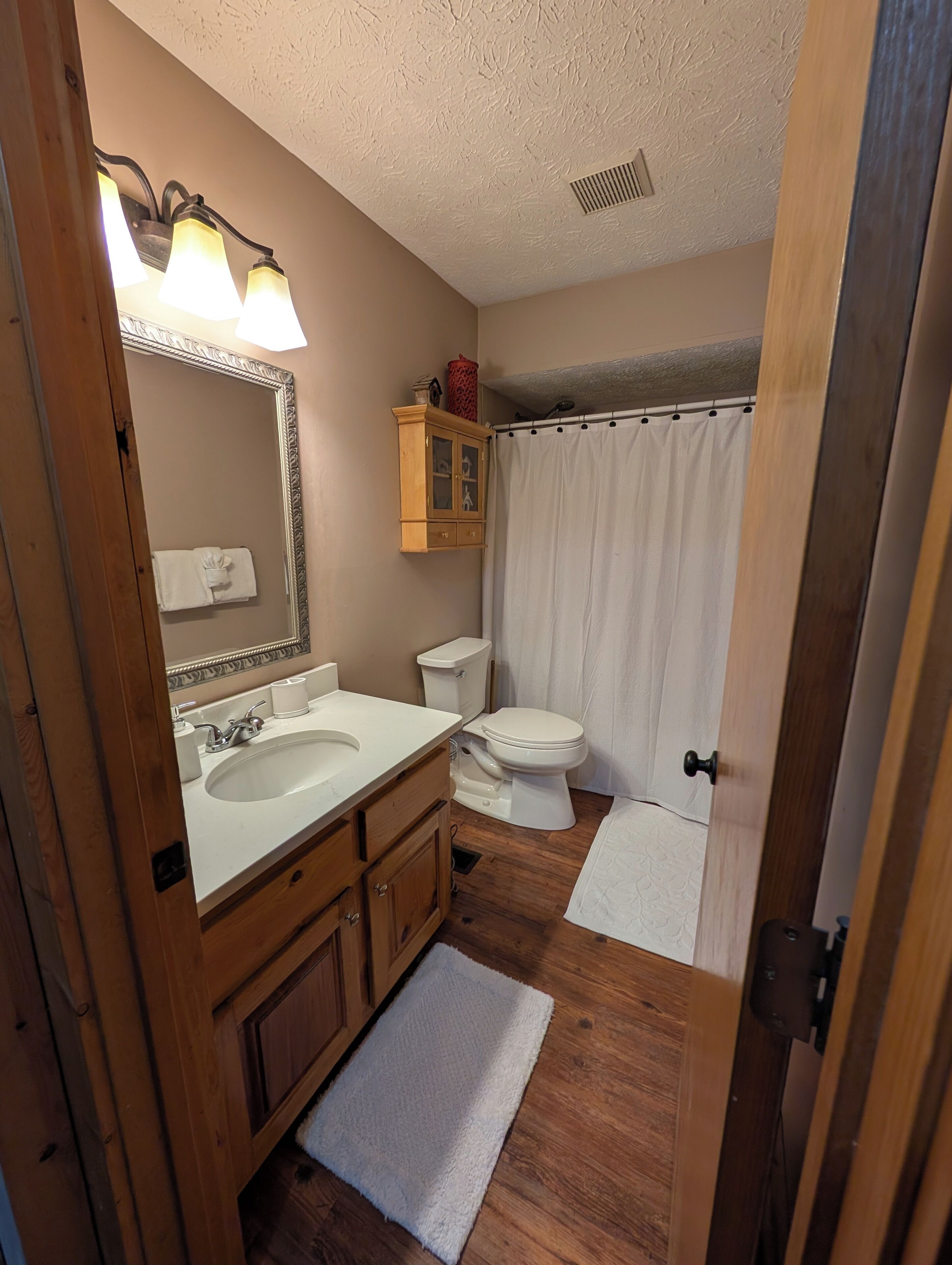 A bathroom with a wooden vanity, a sink, a toilet, and a shower curtain.