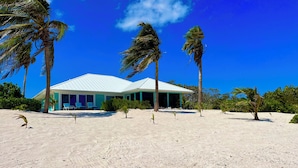 Ein Strandgrundstück mit einem weißen Gebäude, Palmen und einem Sandstrand.