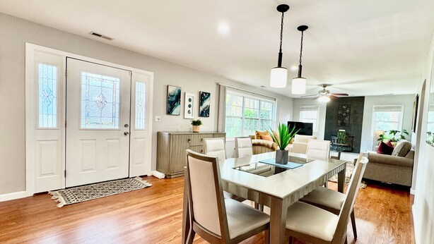 A modern dining area with a wooden table and chairs, a kitchen in the background, and a living area with a sofa and a TV. - Five Star Home 2 miles from Biltmore Estate  (Asheville)