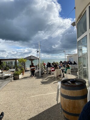 Un espace extérieur aménagé avec des tables et des chaises, un tonneau en bois et une vue sur la mer.