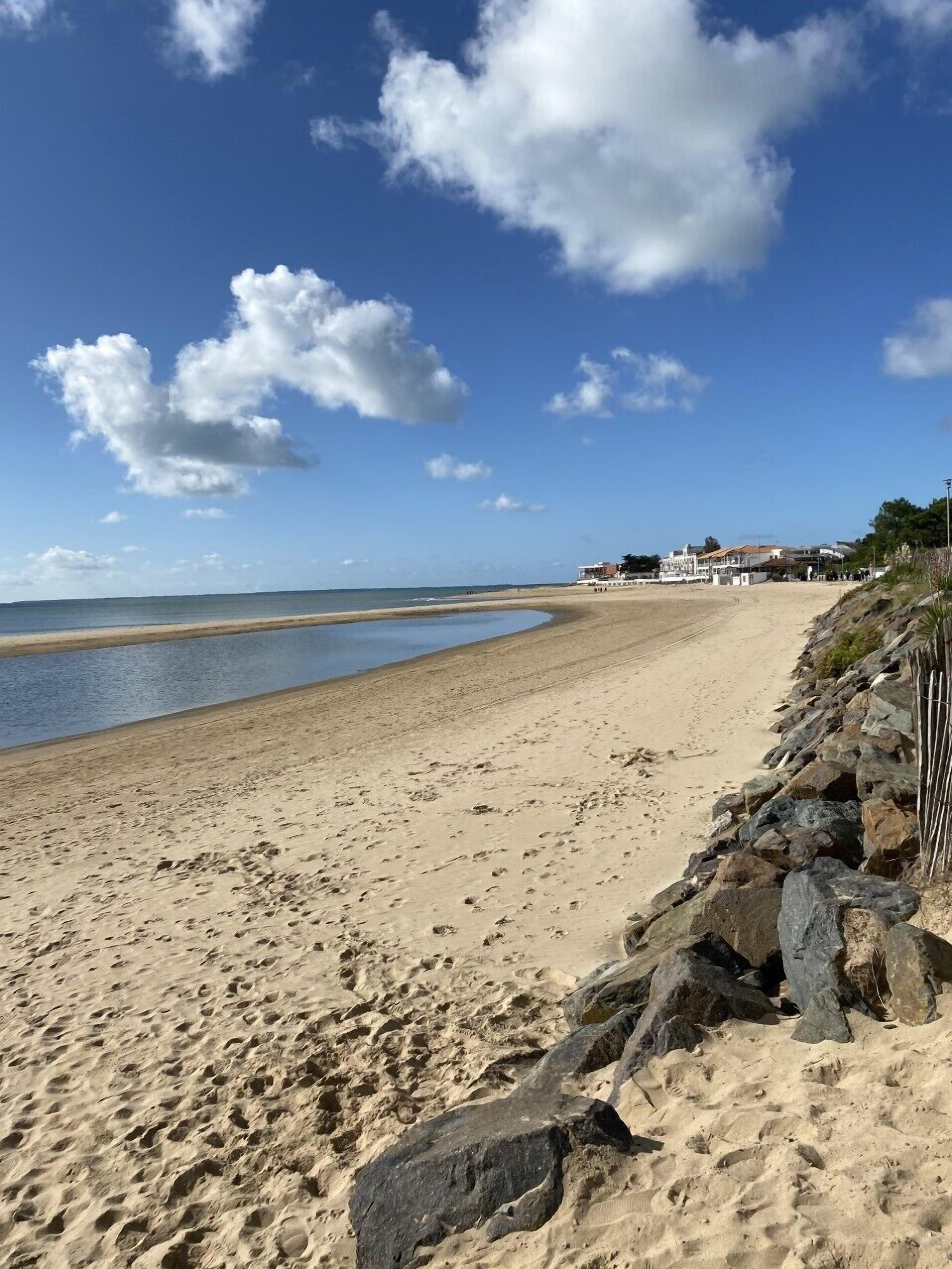 Una playa con costa rocosa, cielo despejado y edificios al fondo.