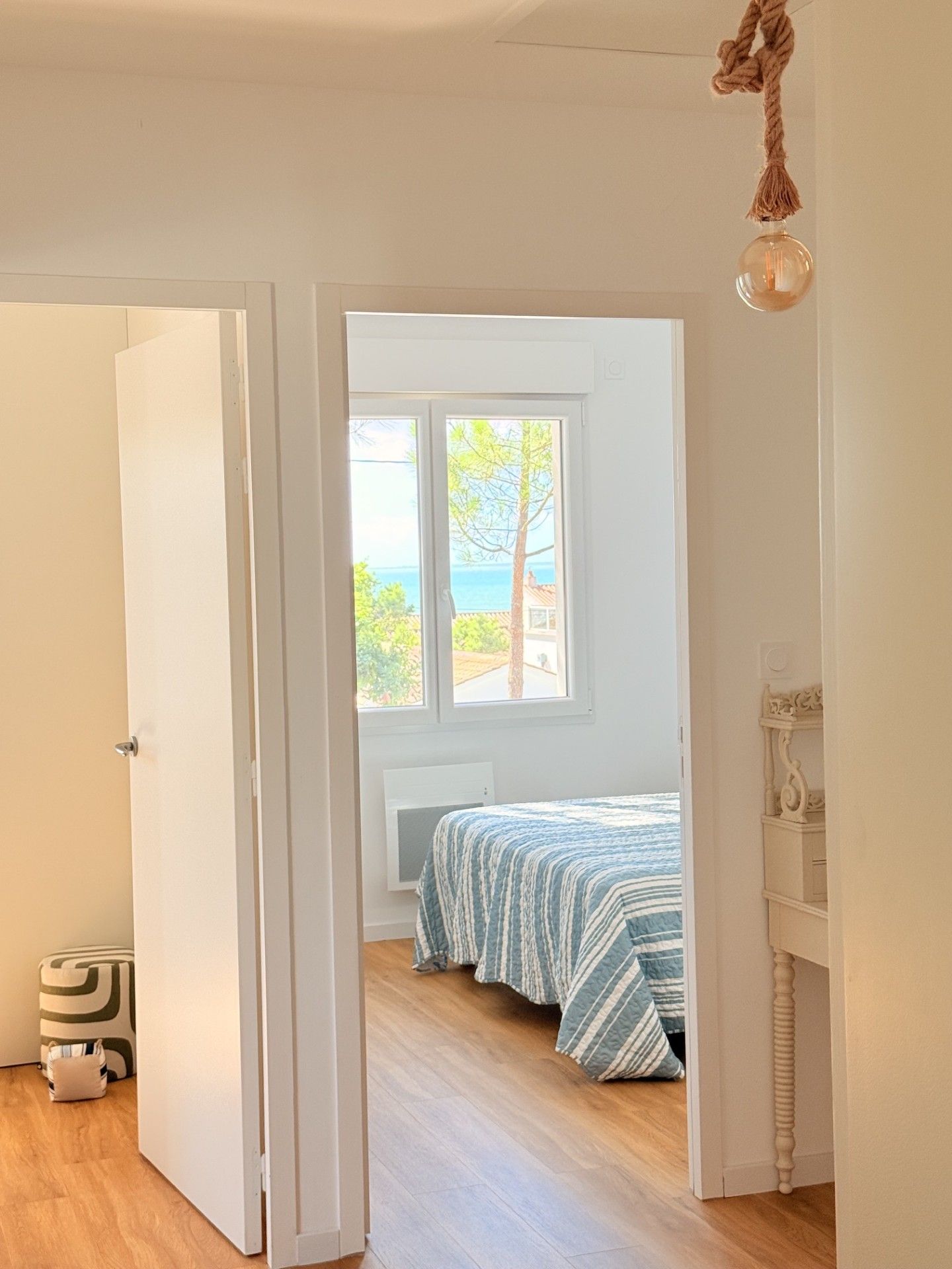 A bedroom with a bed, a window with a view of the sea, and a hanging light fixture.