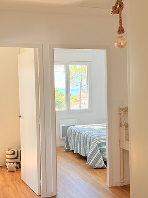 A bedroom with a bed, a window with a view of the sea, and a hanging light fixture.