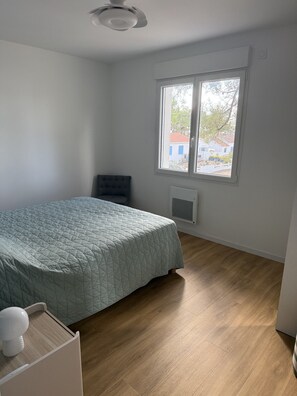 Un dormitorio con cama, una silla, un ventanal y un radiador.
