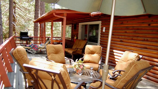 Une terrasse en bois aménagée avec du mobilier d’extérieur, notamment des chaises et une table, ainsi qu’un barbecue.