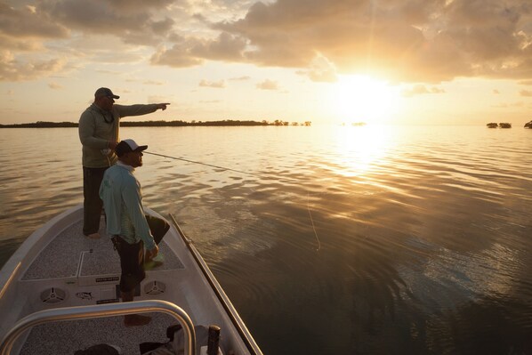 A boat with two people fishing, a clear sky, and a sunset.