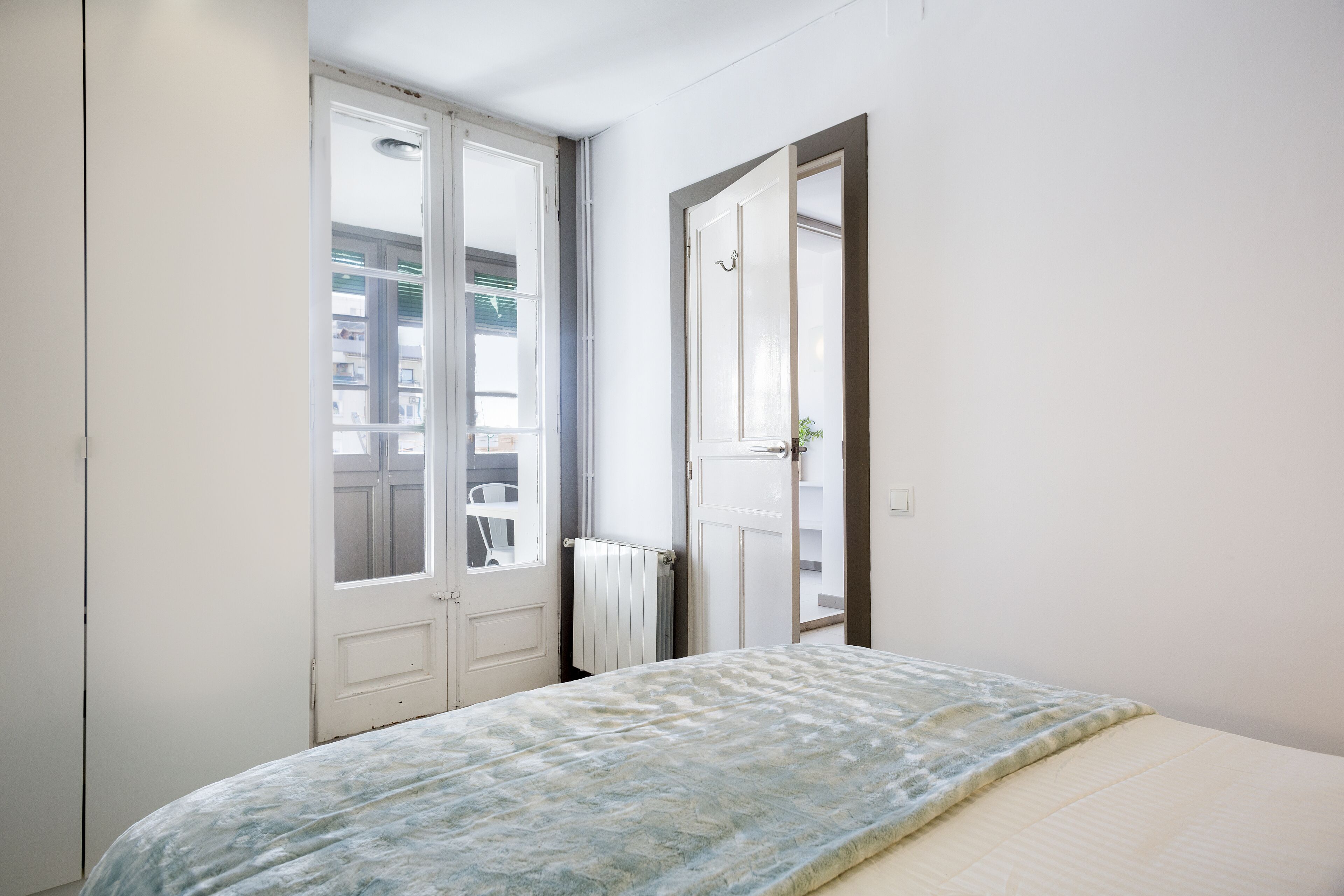Un dormitorio con cama, un radiador y una puerta que da a un balcón exterior.