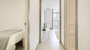 A narrow hallway leading to a bedroom with a bed and a desk.