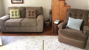 Een woonkamer met een bruine bank, een bruine fauteuil en een ruw bewerkt, wit tapijt.