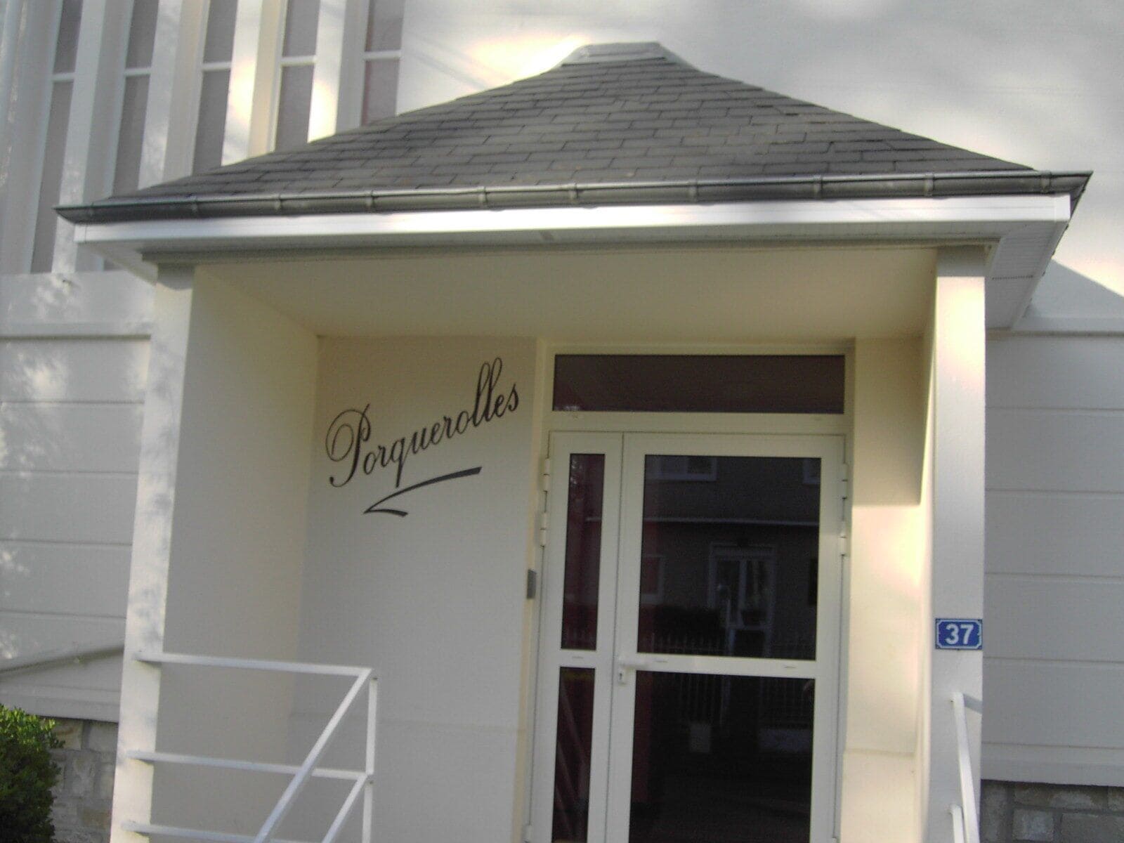 Entrada de un edificio con un letrero que dice "Porqueroles" y un cartel azul con el número "37".
