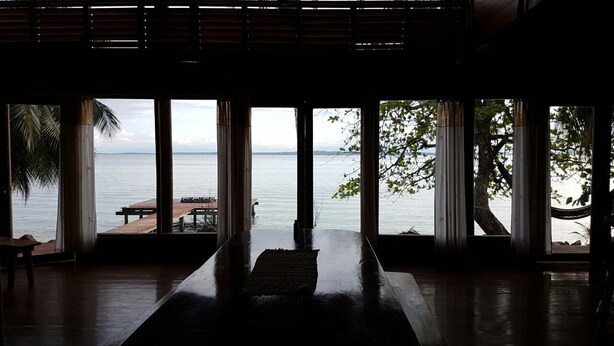 A room with large windows overlooking a body of water, a wooden table, and a bench. - The Ultimate Beach House (Casa Sol Y La Luna) (Bocas Del Toro)