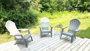 Terraza de madera con tres sillas Adirondack y una mesita.